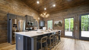 Una cocina moderna con una isla grande, electrodomésticos de acero inoxidable y vistas al bosque a través de amplios ventanales.