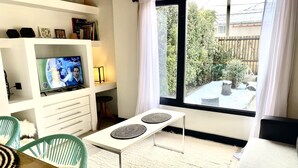 Ein modernes Wohnzimmer mit Fernseher, einer Essecke mit Tisch und Stühlen und einem großen Fenster mit Gartenblick.