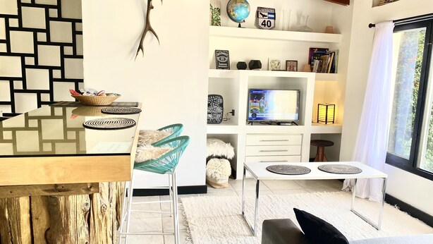 Ein modernes Wohnzimmer mit einem Glastisch, einem Holzesstisch, einer Couch und einem Fernseher auf einem weißen Schrank.