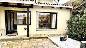 Eine terrasse mit Steinpflasterung, bedeckt mit Schnee, eine Holztür und ein Fenster mit Blick auf ein Gebäude im Hintergrund.