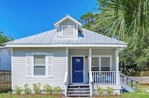 A single-story house with a blue front door, white shutters, and a small porch with a white railing.