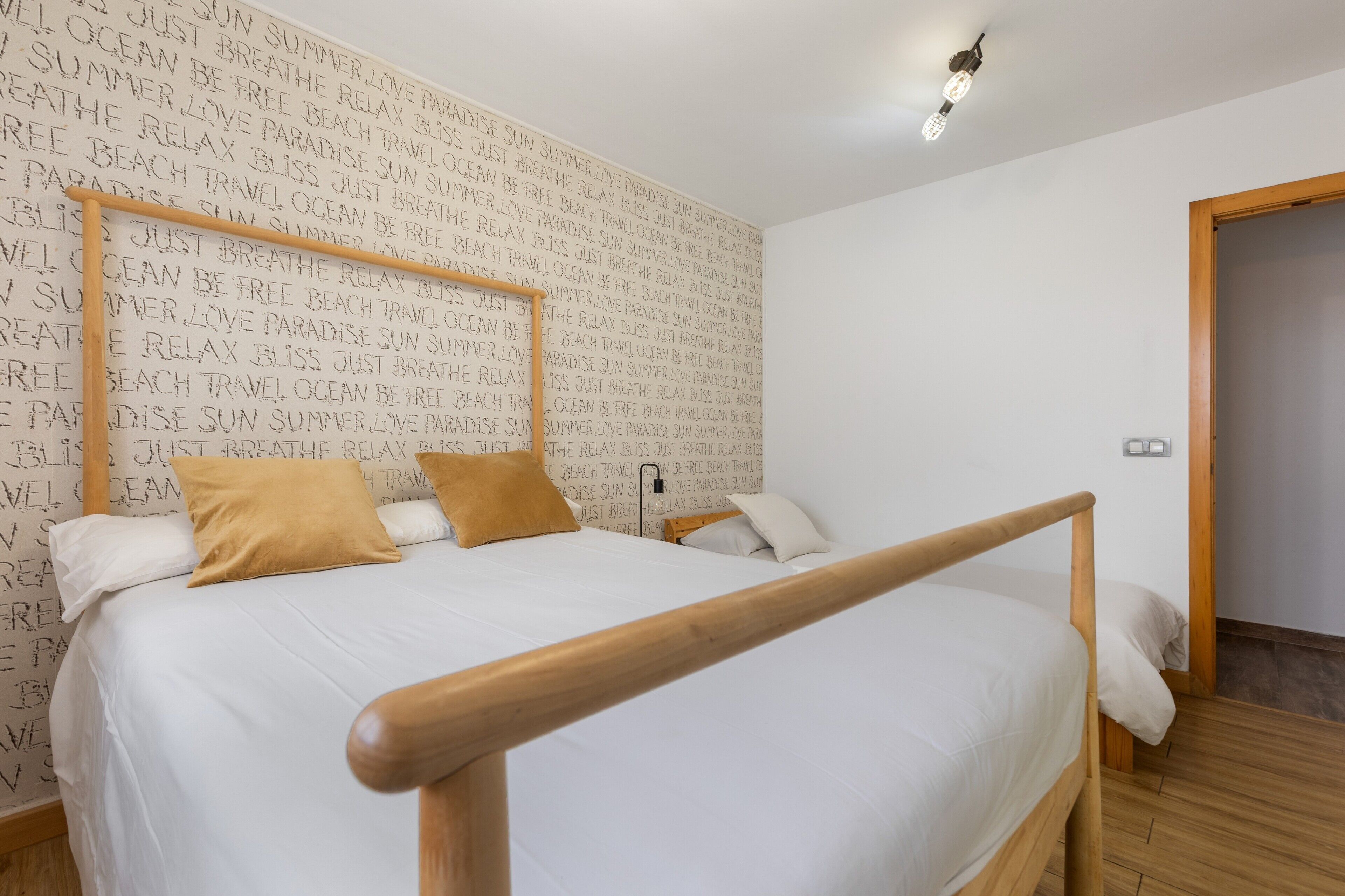 Un dormitorio con estructura de cama de madera, ropa de cama blanca y una pared con texto repetido.