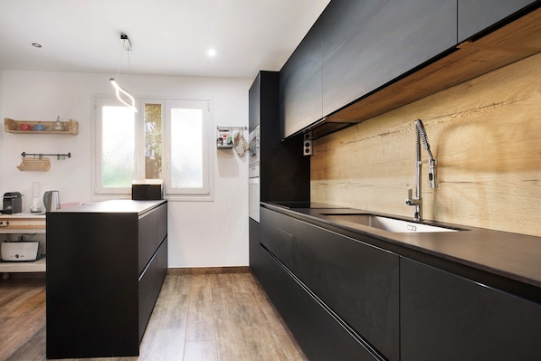 A modern kitchen with a wooden backsplash, black cabinetry, and a stainless steel sink. - 'Villa del Relax' with Sea Views, Pool, and Wi-Fi (Corralejo)
