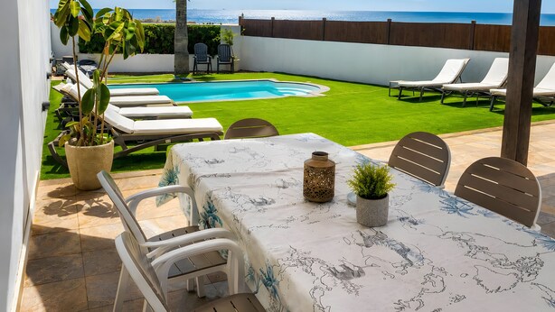 Uma área à beira da piscina com vista para o mar, uma mesa com toalha e cadeiras de descanso.