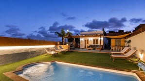 Uma piscina com espreguiçadeiras, uma área de estar coberta e uma parede de madeira.