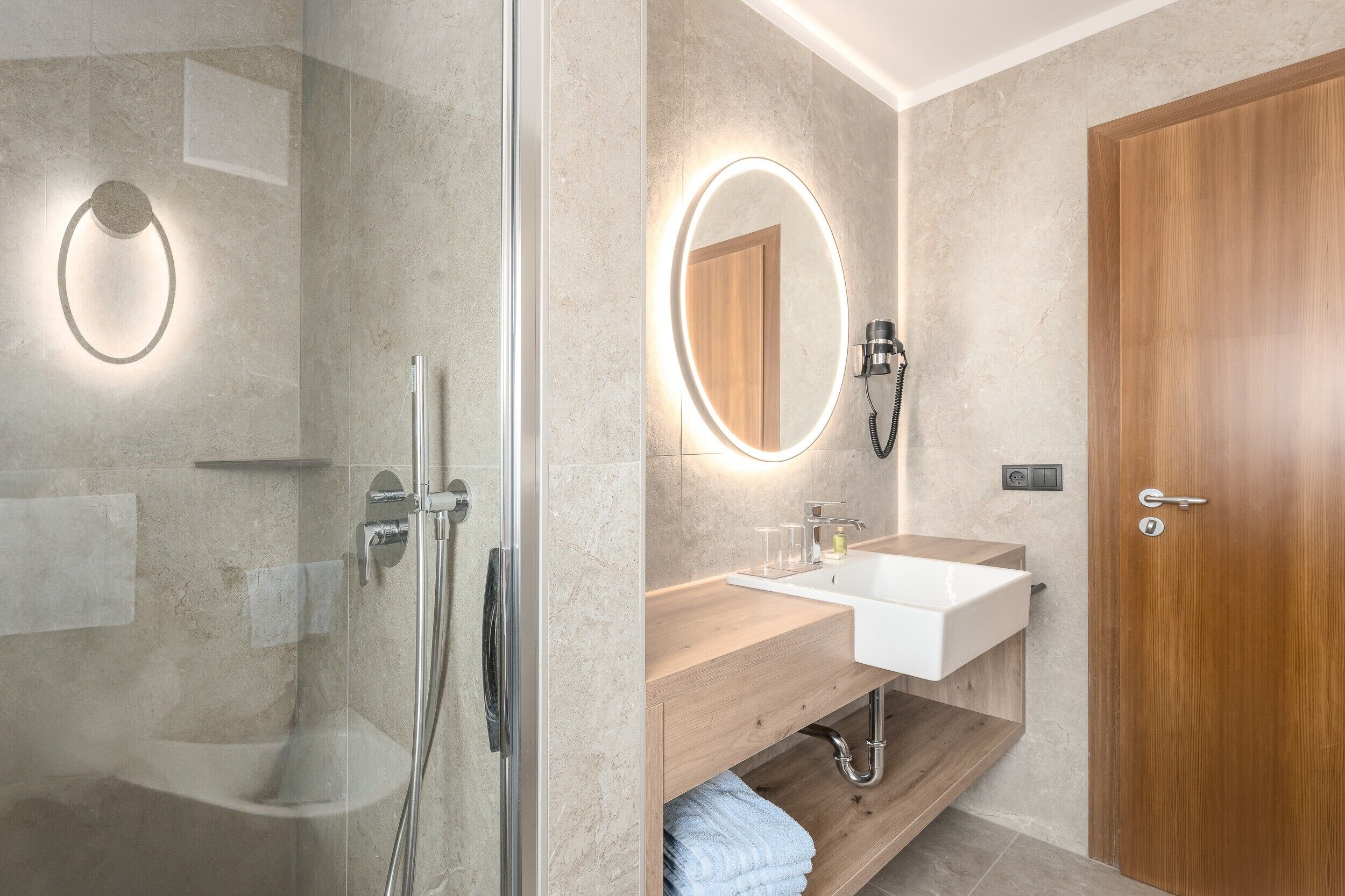 A modern bathroom with a glass-enclosed shower, a wooden vanity with a white sink, and a wooden door.