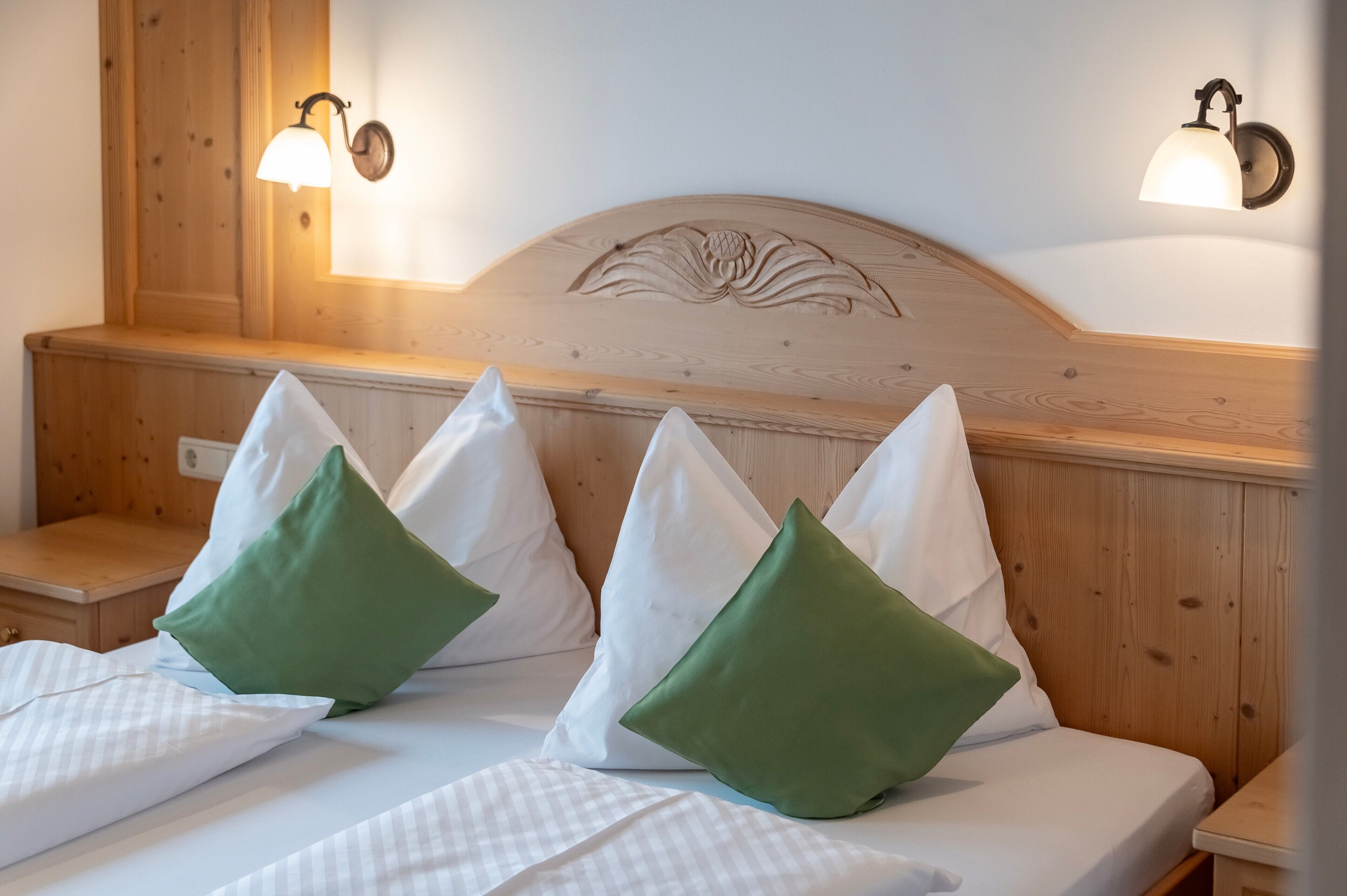 Habitación de hotel con cabecera de madera, dos mesitas de noche y cama con ropa de cama blanca y almohadas verdes.