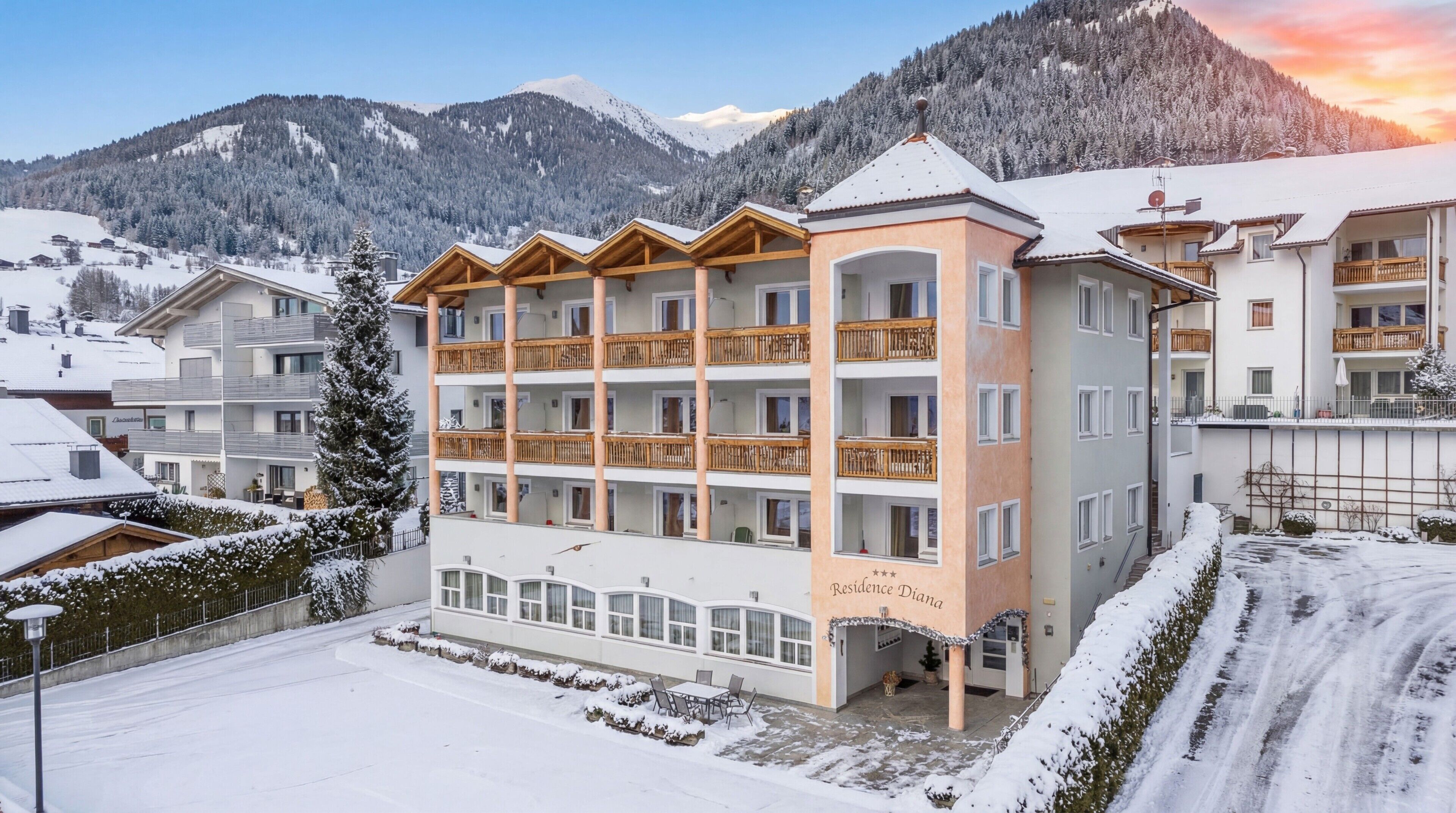 Un hotel de varios pisos con balcones, un área de estar al aire libre techada y vistas a montañas nevadas.