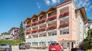 Een hotel met meerdere verdiepingen, voorzien van balkons met bloemen, een heldere lucht en geparkeerde auto's.