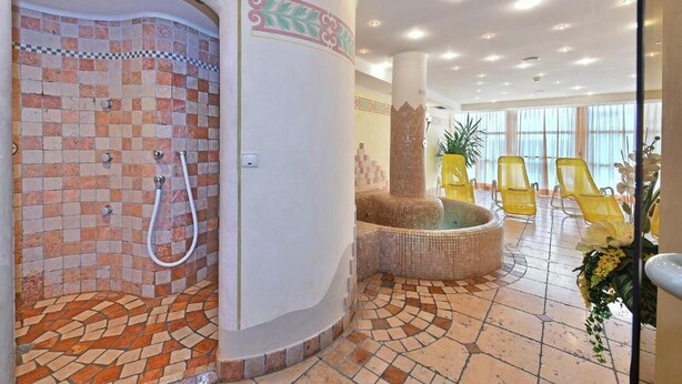 Un espace spa comprenant une douche aux murs recouverts de mosaïques, un jacuzzi et des chaises jaunes.