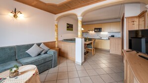 Un salon comprenant un canapé, une table basse et un meuble pour la télévision. Il y a également un coin cuisine avec une table à manger et des chaises.