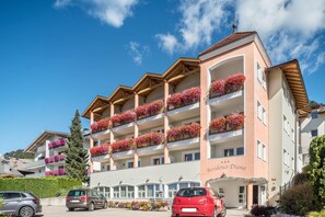 Un hôtel à plusieurs étages, doté de balcons ornés de fleurs, sous un ciel dégagé, avec des voitures garées.