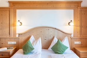 A wooden headboard with two wall-mounted lamps, a bed with white bedding and green pillows, and a nightstand with a book and a drawer.