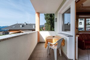 Un balcón con mesa y silla, vistas del barrio y un sofá rojo en el interior.