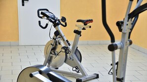 Un vélo d’appartement dans une pièce dont le sol est recouvert de carreaux et qui possède un mur uni.