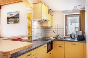 Une cuisine avec des meubles de couleur jaune, un évier en acier inoxydable et une fenêtre avec des rideaux.