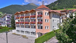 Un hôtel à plusieurs étages doté de balcons ornés de fleurs, d’un parking et surplombant un paysage montagneux.