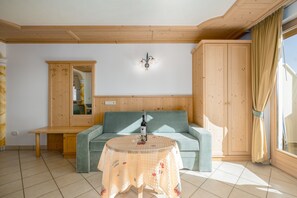 Une pièce avec un plafond en bois, un canapé, une table recouverte d’une nappe et une armoire.