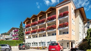 A multi-story hotel with balconies adorned with flowers, a clear blue sky, and parked cars in the foreground. - 'Residence Diana Apartment 301' with Mountain View, Balcony & Wi-Fi (Terenten)