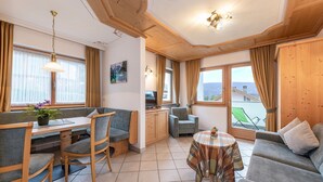 Una habitación acogedora con una mesa de comedor, sillas, un sofá, una mesita con mantel a cuadros y vistas al exterior.
