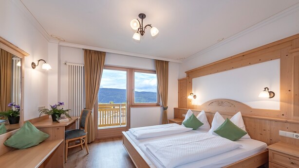 Habitación de hotel con una cama grande, un escritorio, una silla, un ventanal con vistas y un cabecero de madera.