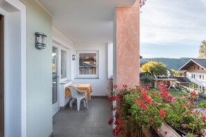 En balkon med et bord og stole, et vindue og udsigt til en have og huse.