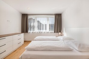 Une chambre à coucher avec un lit, une table de chevet, une fenêtre avec des rideaux et une prise électrique au mur.