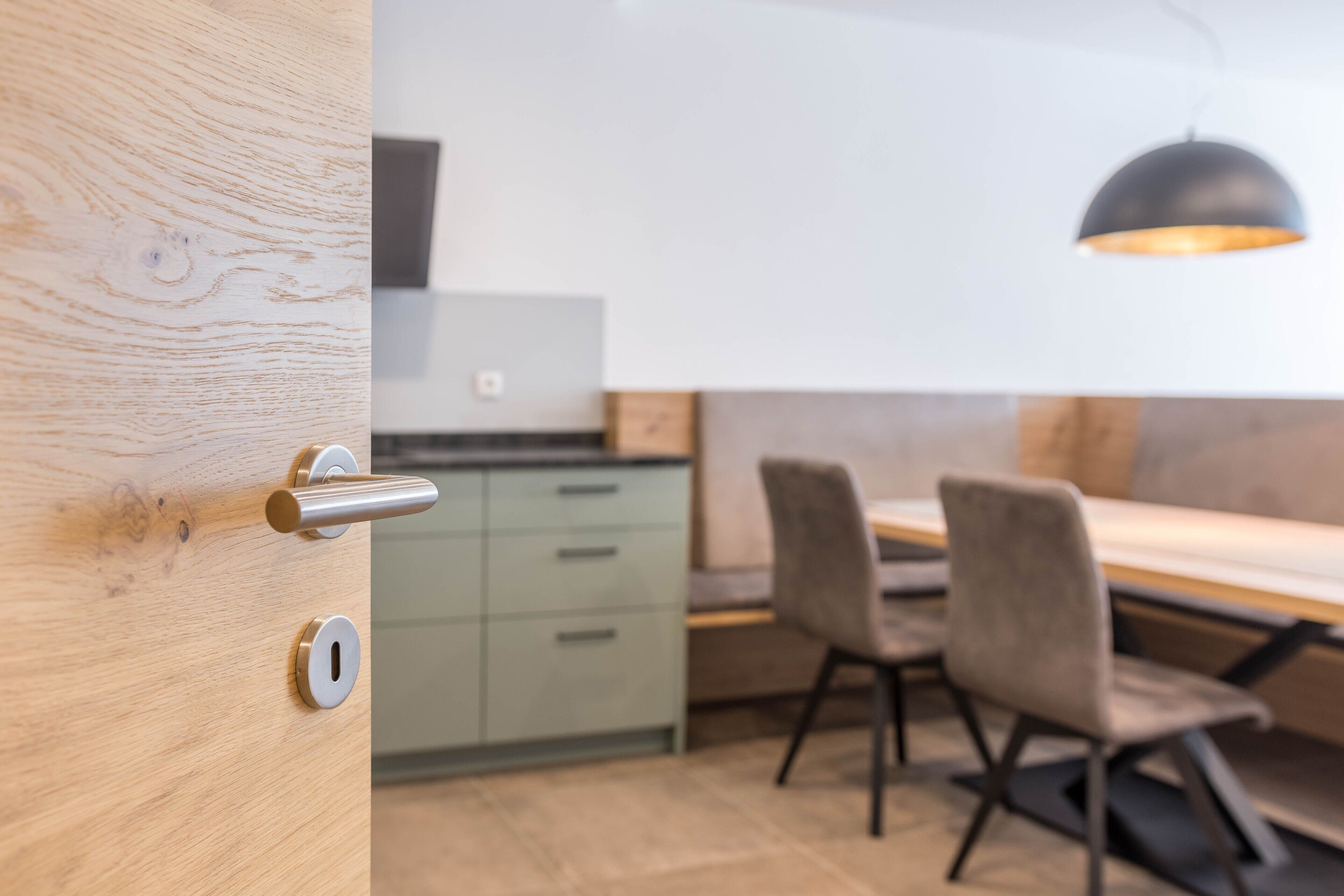 A modern kitchen with a wooden door, a dining area with a table and chairs, and a pendant light.