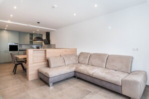 Un salon moderne comprenant un canapé d’angle, un coin repas et une cuisine équipée d’appareils électroménagers intégrés.