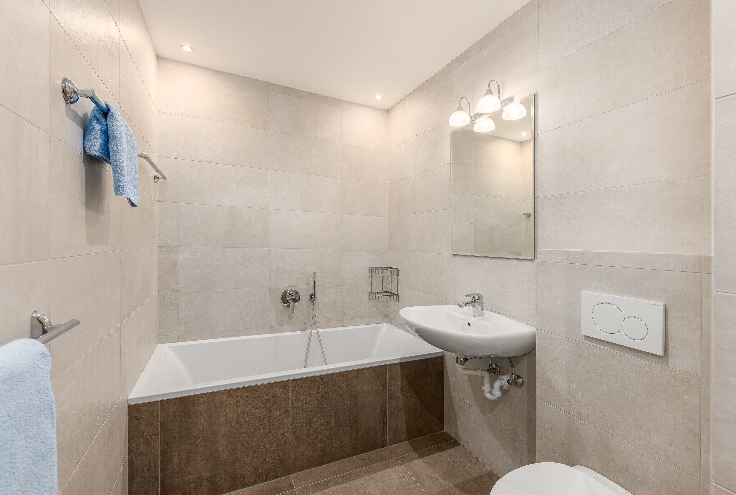 Une salle de bain moderne équipée d’une baignoire, d’une douche et d’un lavabo, avec un miroir et un éclairage encastré.