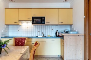 Une cuisine compacte avec des meubles de couleur jaune, un four à micro-ondes, un évier et un coin repas comprenant une table et des chaises.