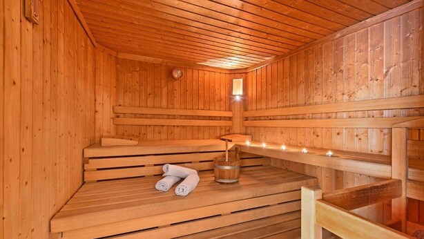 Eine Holzsauna mit Bänken, einem Eimer und einer Uhr an der Wand.