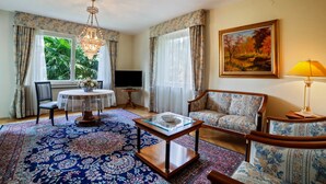 A living room with a round table, two sofas, a chandelier, and a painting on the wall. - Villa Coris Apartment Magnolia 110 sqm with Garden (Merano)