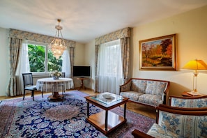 A living room with a round table, two sofas, a chandelier, and a painting on the wall.