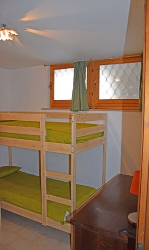 Ein Etagenbett mit Fenster darüber, ein Holztisch und ein kleiner, orangefarbener Mülleimer.