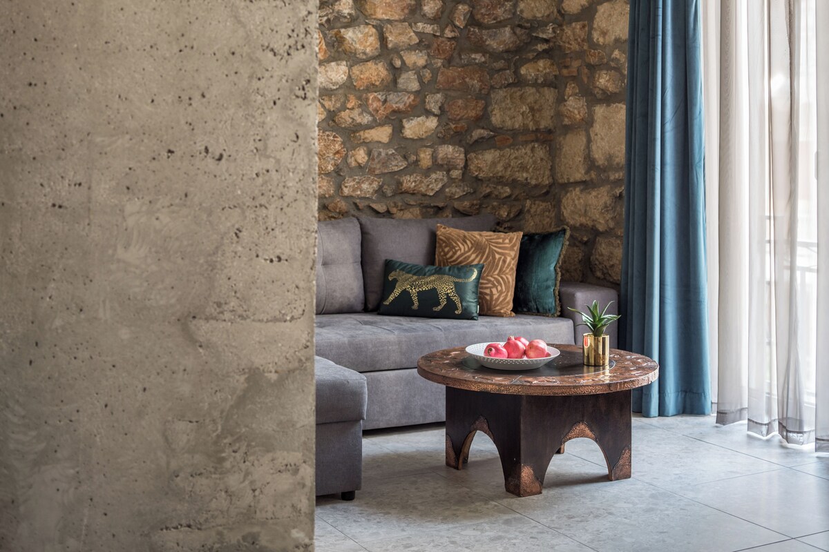 A living room with a stone wall, grey sofa, and a round coffee table with a bowl and decorative items.