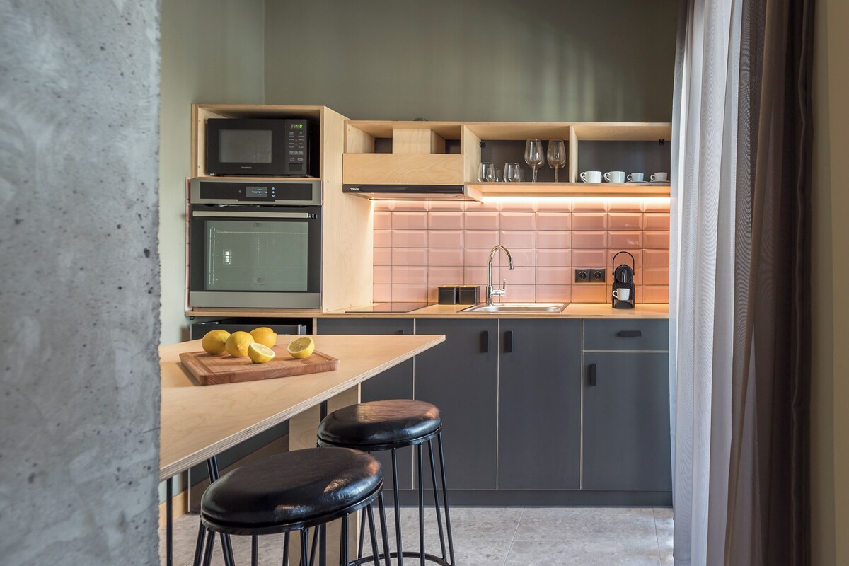 A modern kitchen with a wooden countertop, two stools, a cutting board with lemons, a microwave, an oven, and a sink.