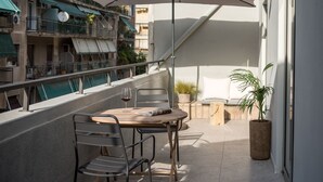 A balcony with a round table and chairs, a white umbrella, and a potted plant. - Cohort Koukaki (Athens)