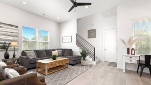Ein geräumiges Wohnzimmer mit grauem Sofa, einem Holztisch und einer Treppe, die in ein Obergeschoss führt.