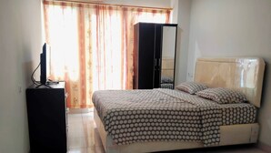 A bedroom with a bed, a television on a stand, a wardrobe, and a window with curtains. - S&A Property 4 (Citaringgul)