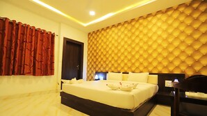 Quarto de hotel com uma cama grande, cabeceira com desenho em padrão losango, mesa de cabeceira de madeira e cortina vermelha.