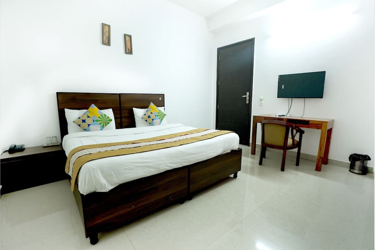 A bedroom with a bed, a desk, a chair, a TV, and a door.