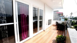 Un balcón con suelo de madera, puertas de cristal correderas amplias y vista panorámica de la ciudad.