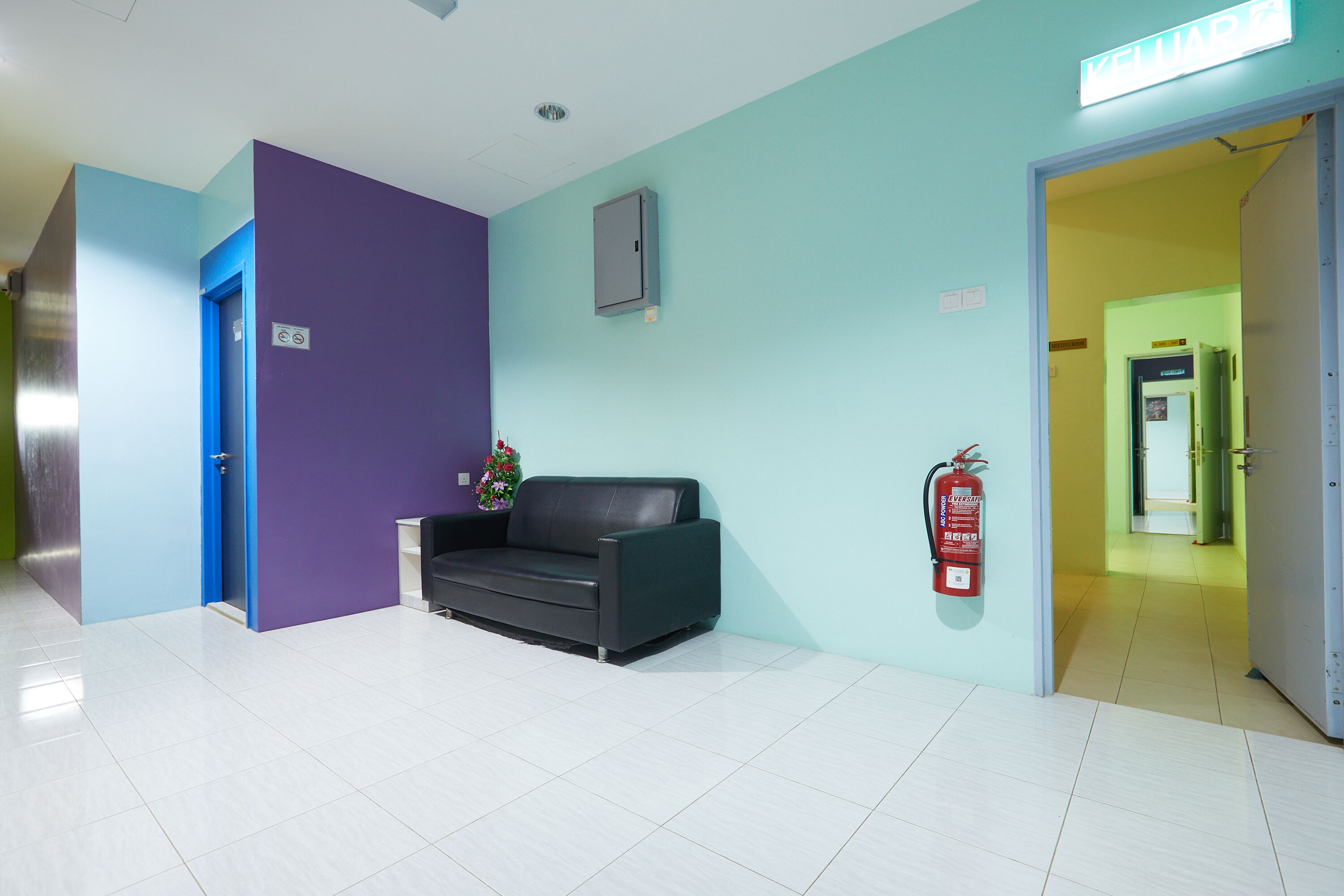 A reception area with a black sofa, a fire extinguisher, and a closed door.