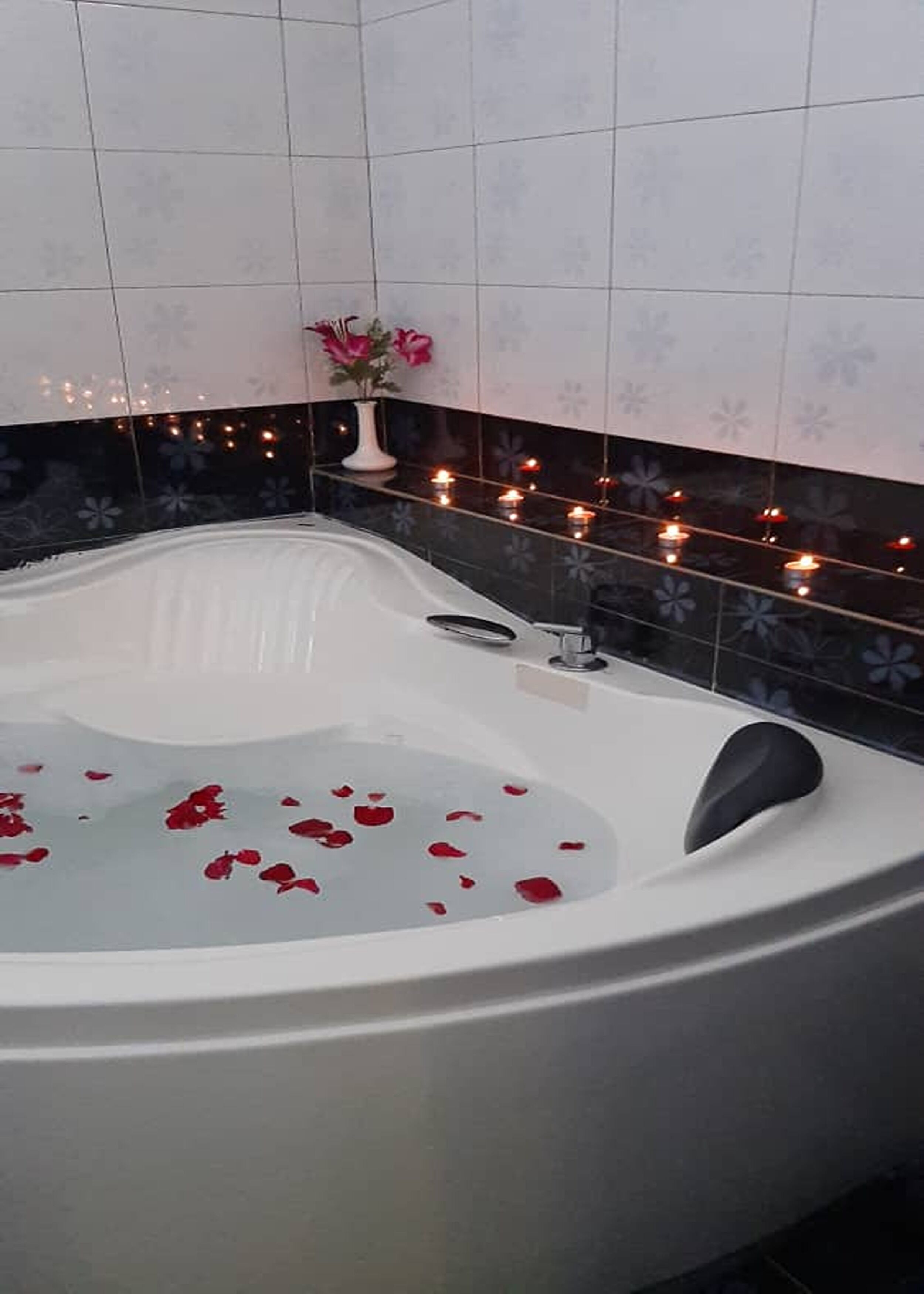 Una bañera con pétalos de rosa, un florero con flores y velas a un lado.