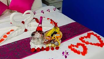Relax in comfort with a neatly made bed, featuring a heart-shaped rose petal arrangement, champagne, chocolates, and a fresh banana.