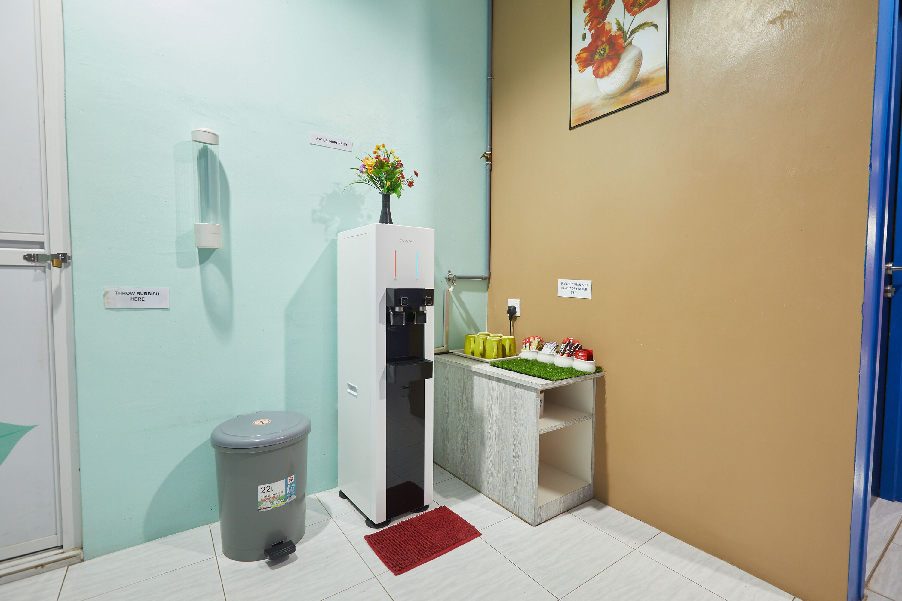 A small bathroom with a water dispenser, a trash bin, and a sink with a green plant on the counter.