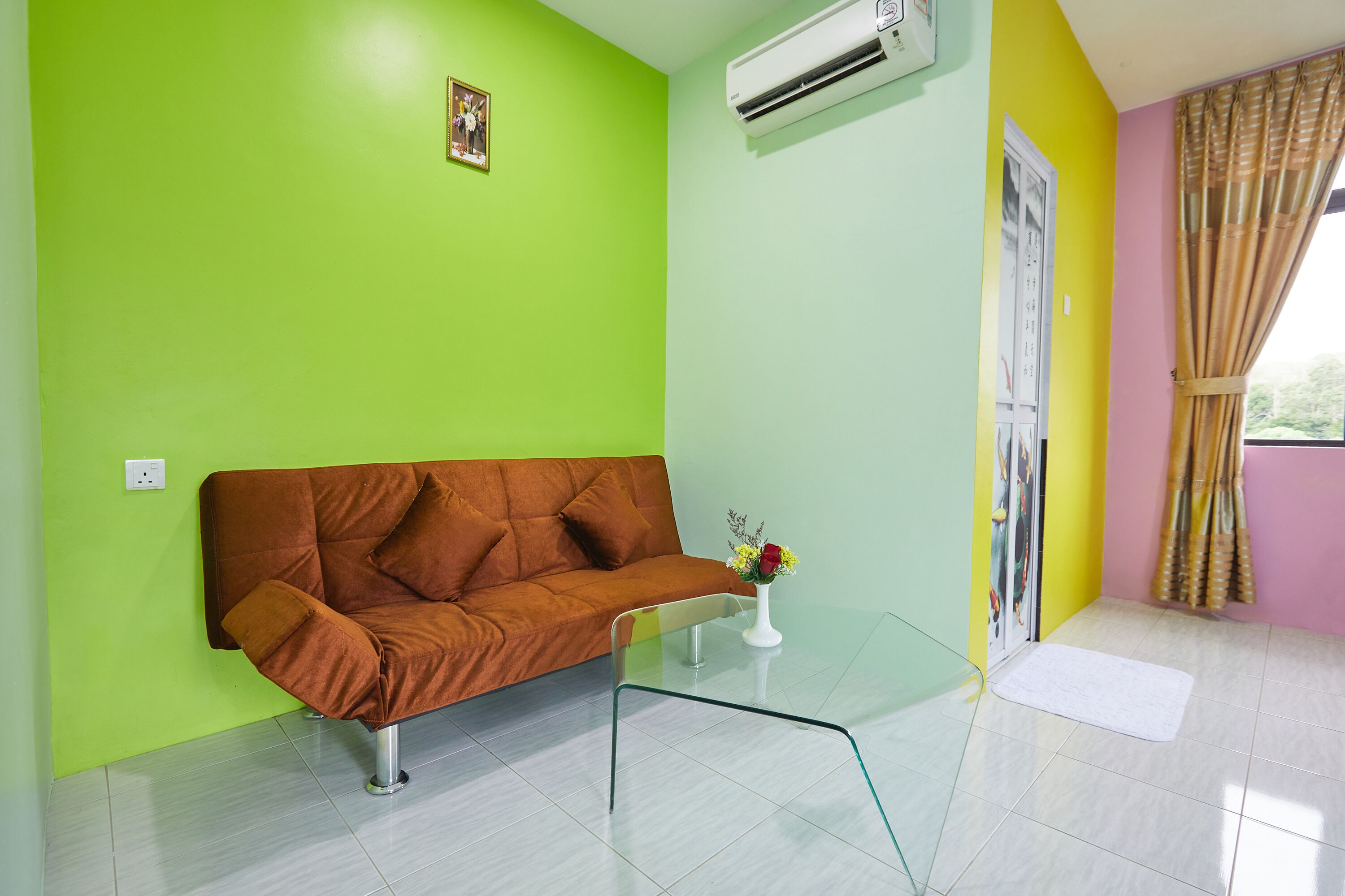 Una habitación con pared verde, sofá marrón, una mesita de cristal con un florero y un aire acondicionado blanco.