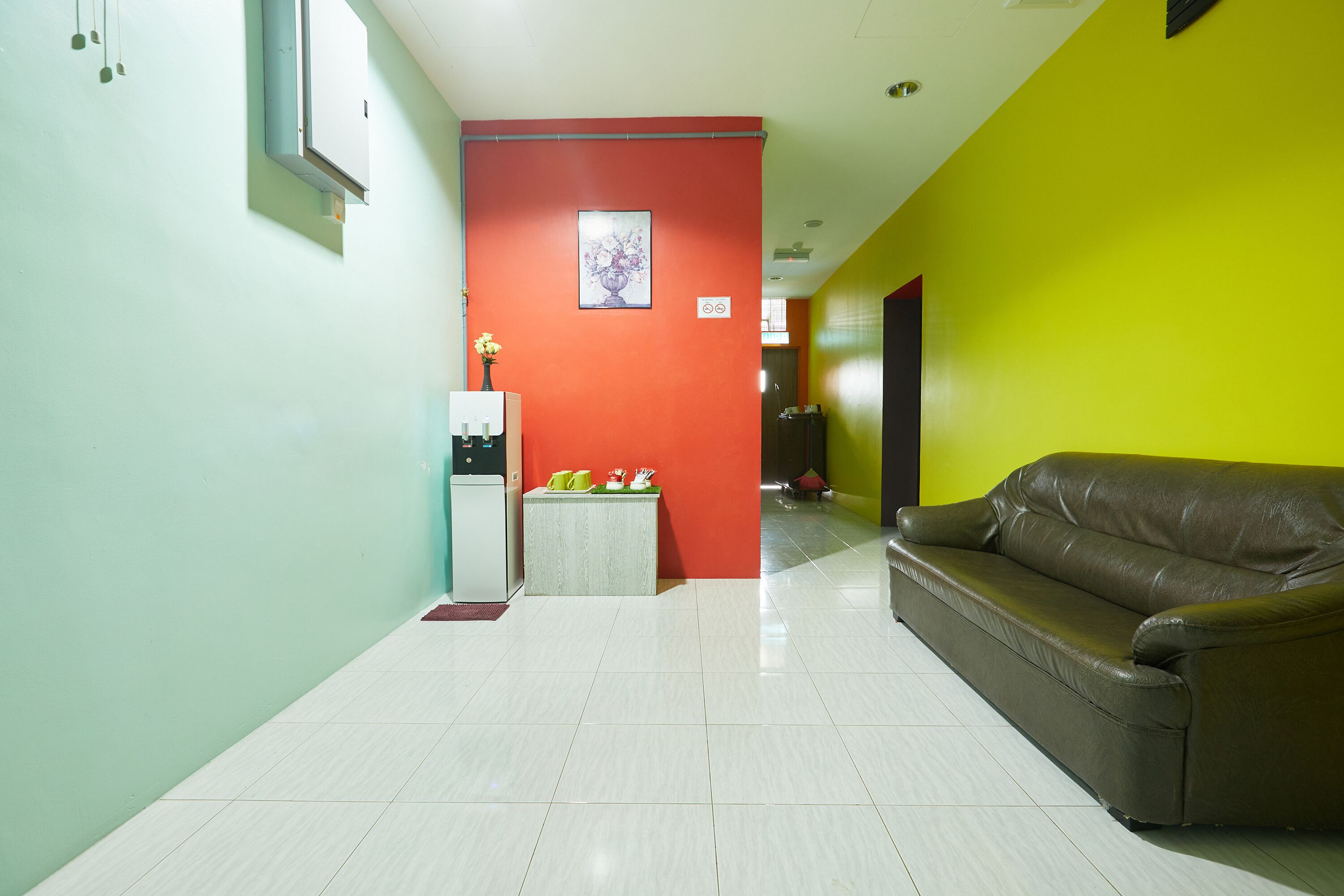 A hallway with a brown leather sofa, a refrigerator, and a small table with a vase and a plant.