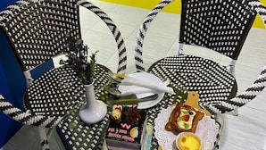 A dining area with two wicker chairs, a small table with a vase of flowers, a cake, and a basket of bread. - Sy Jerantut Hotel (Jerantut)